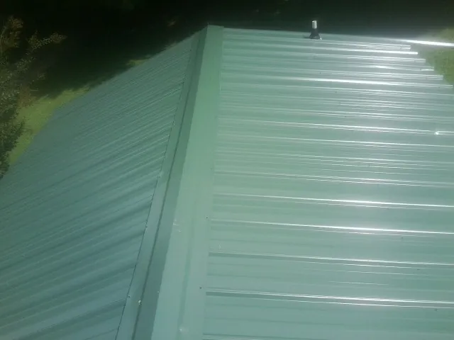 New green metal panels meeting at the ridge of a roof — Flat Roof Repair work by our crew in New Berlin