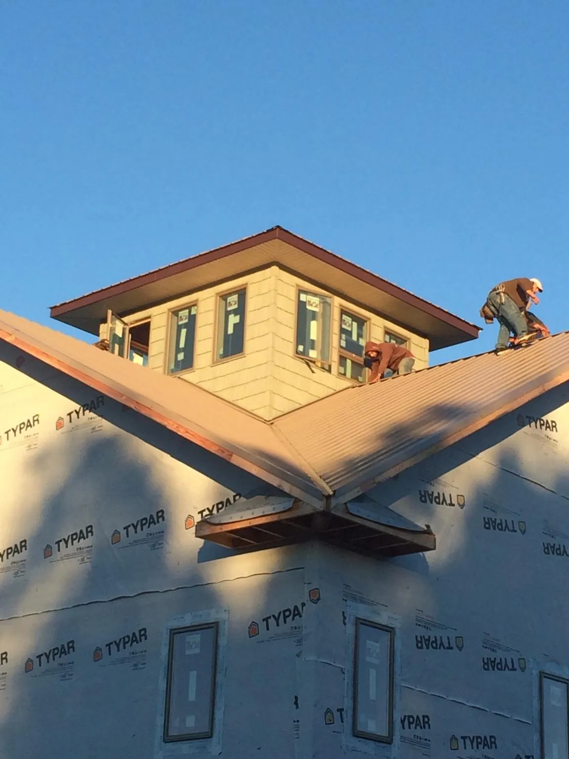 Roofers working around a rooftop cupola on a new metal roof at sunset in New Berlin
